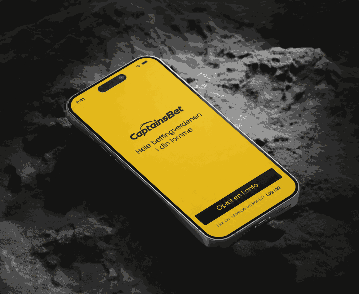 Smartphone med CaptainsBet-appen på en gul skærm og sloganet "Hele bettingens verden i din lomme".